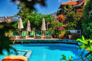 A pool area with lounge chairs and umbrellas, surrounded by lush greenery and a mountain backdrop. - Fidanka Hotel (Kas)