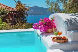A poolside area with a white wall, a basket of pink flowers, and a tray with drinks and fruit. - Fidanka Hotel (Kas)