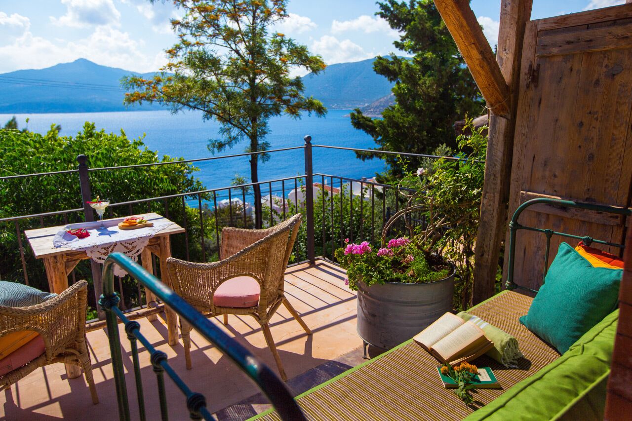 A wooden deck with wicker furniture, a table with a drink, and a potted plant.