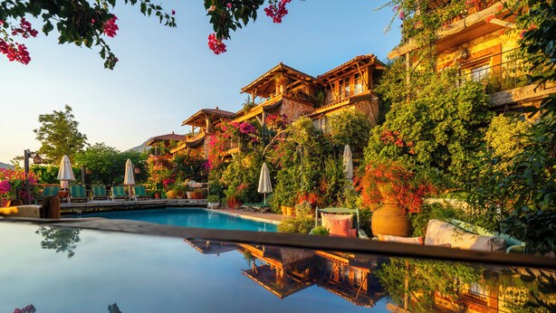 A poolside view of a resort with multiple buildings, lush greenery, and a clear reflection in the water. - Fidanka Hotel (Kas)