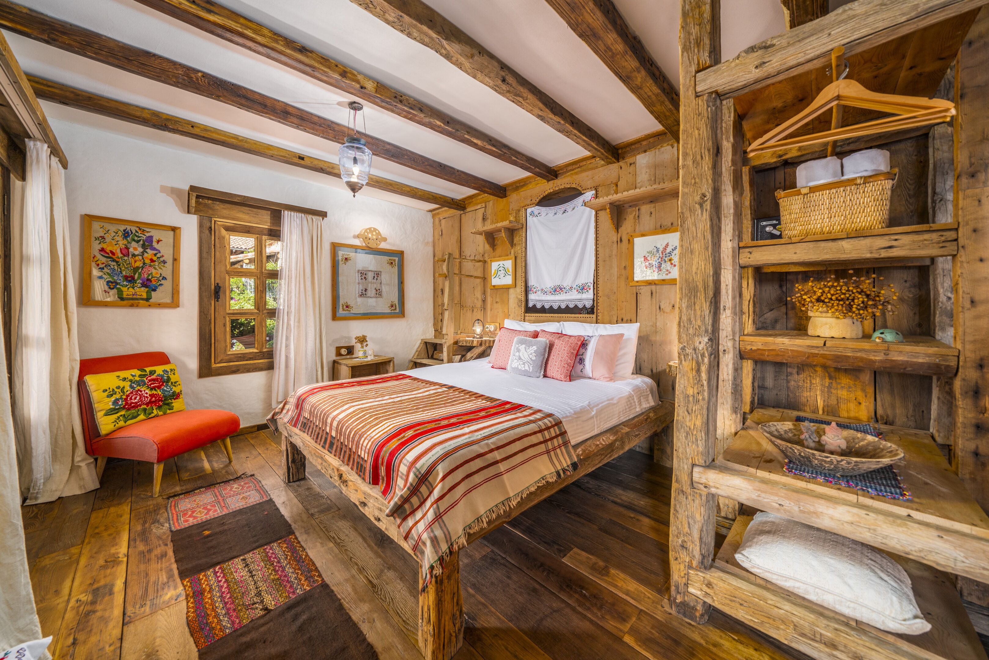 A rustic bedroom with a wooden bed, a red chair, and a wooden shelf with baskets.