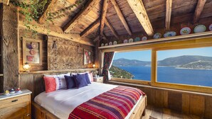 A rustic wooden bedroom with a large bed, a wooden dresser, and a view of the sea. - Fidanka Hotel (Kas)