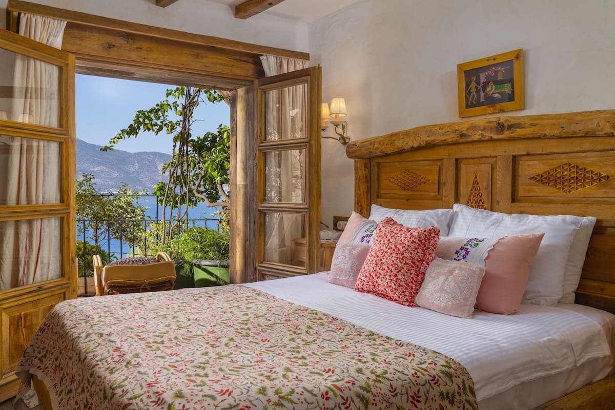 A bedroom with a large bed, floral bedding, a view of mountains, and a balcony with plants.