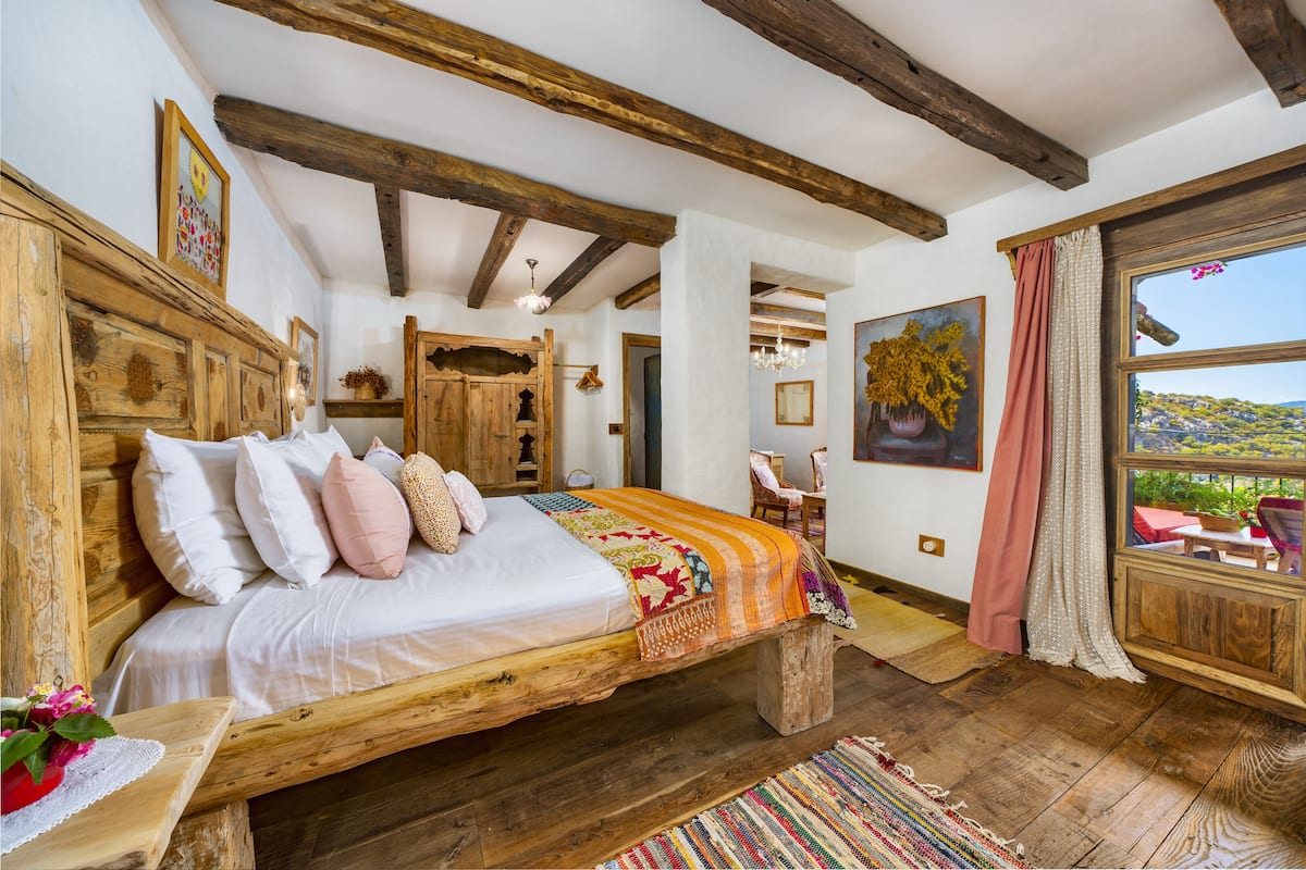 A rustic bedroom with a wooden bed, a large window with a view, and a chandelier.