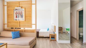 A modern hotel room with a sofa, a bed, a small table, a mirror, and a wooden partition with artwork.