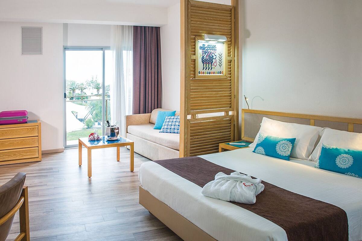 A hotel room with a bed, a sofa, a wooden dresser, a table, and a chair.