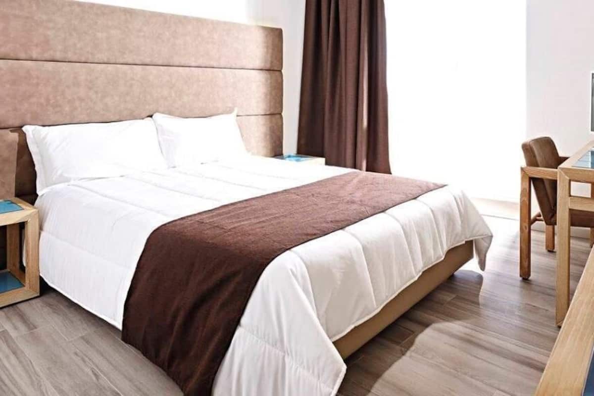 A hotel room with a large bed, a wooden nightstand, a desk with a chair, and a television.