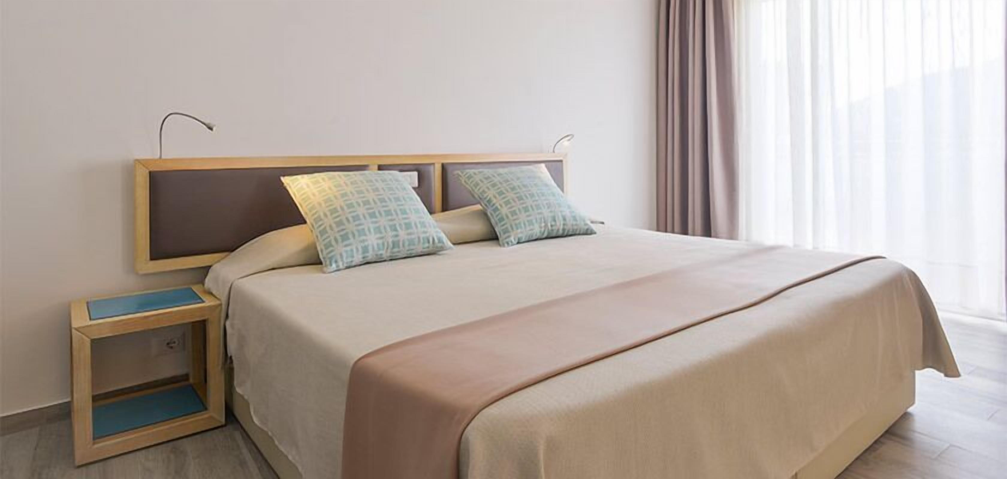 A neatly made bed with a headboard, two pillows, and a bedside table with a lamp.