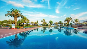 A large outdoor swimming pool with palm trees and umbrellas, surrounded by a paved walkway. - Hotel Baia Di Conte (Alghero)