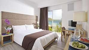 A hotel room with a large bed, a desk with a laptop, a TV, and a view of the sea. - Hotel Baia Di Conte (Alghero)