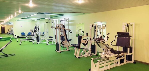 A gym with various exercise machines, green carpet, and mirrors on the walls. - Hotel Baia Di Conte (Alghero)