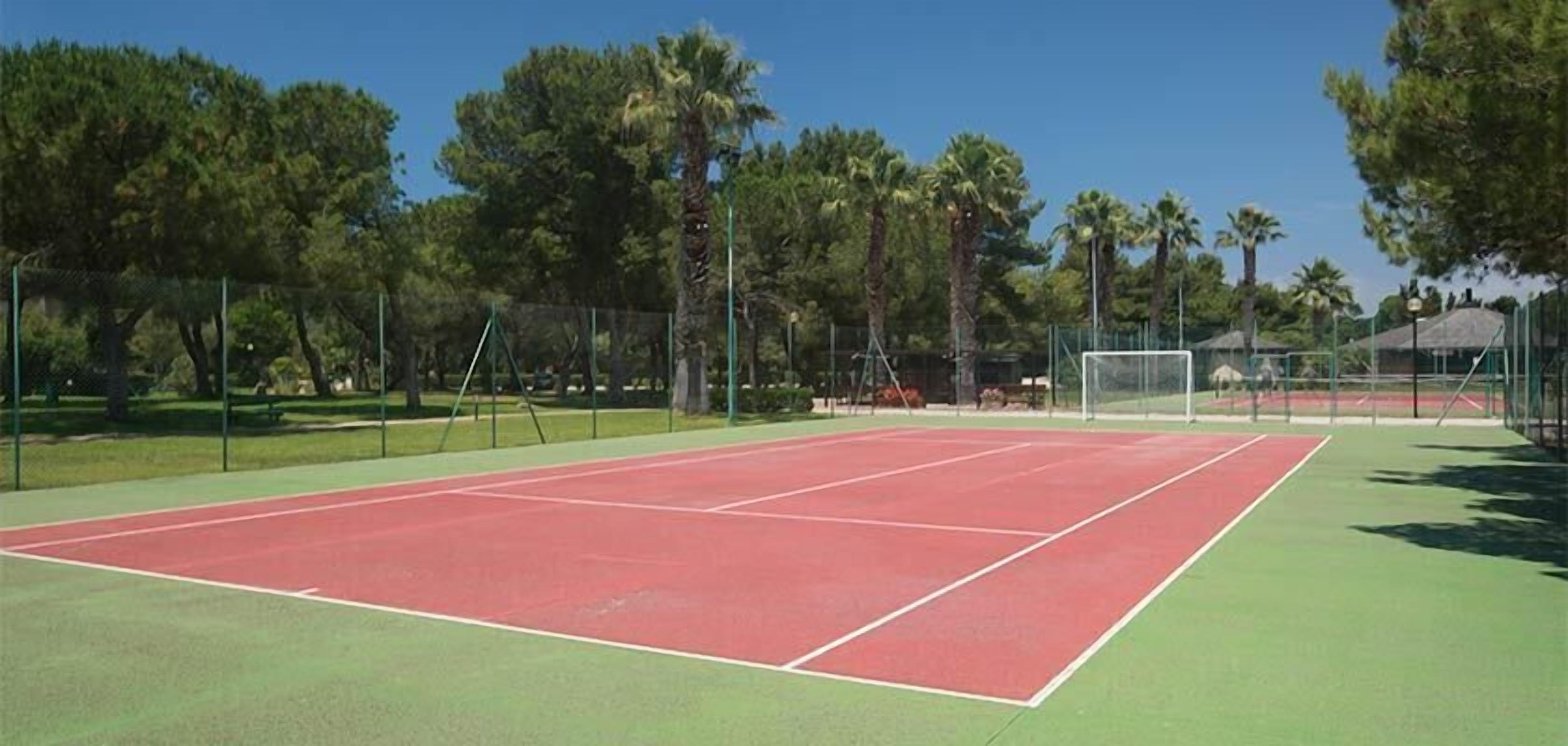 Ein Tennisplatz mit roter und grüner Belagaung, umgeben von Bäumen und einem Zaun.