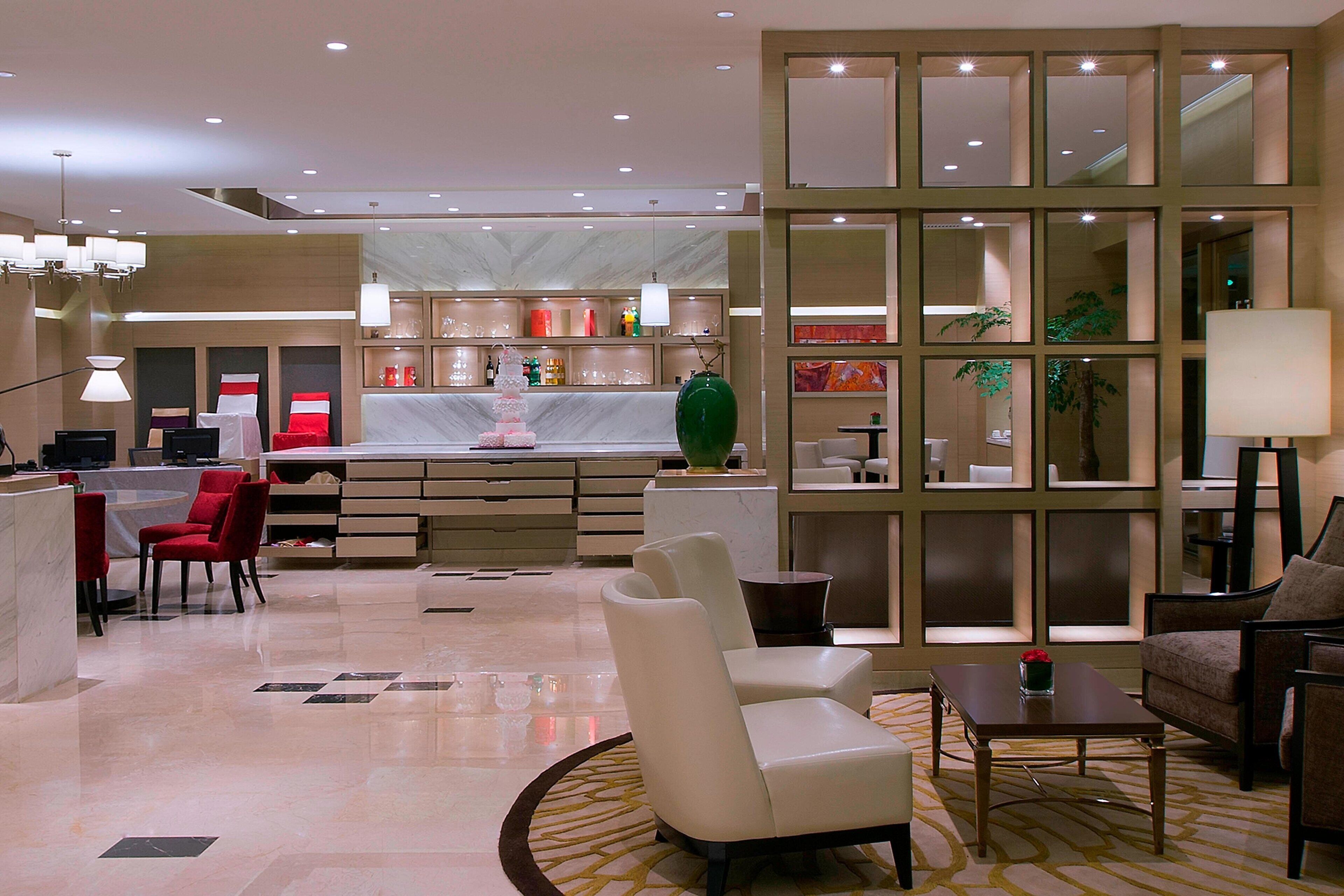 A modern hotel lobby with a reception desk, seating area, and a large mirror wall.