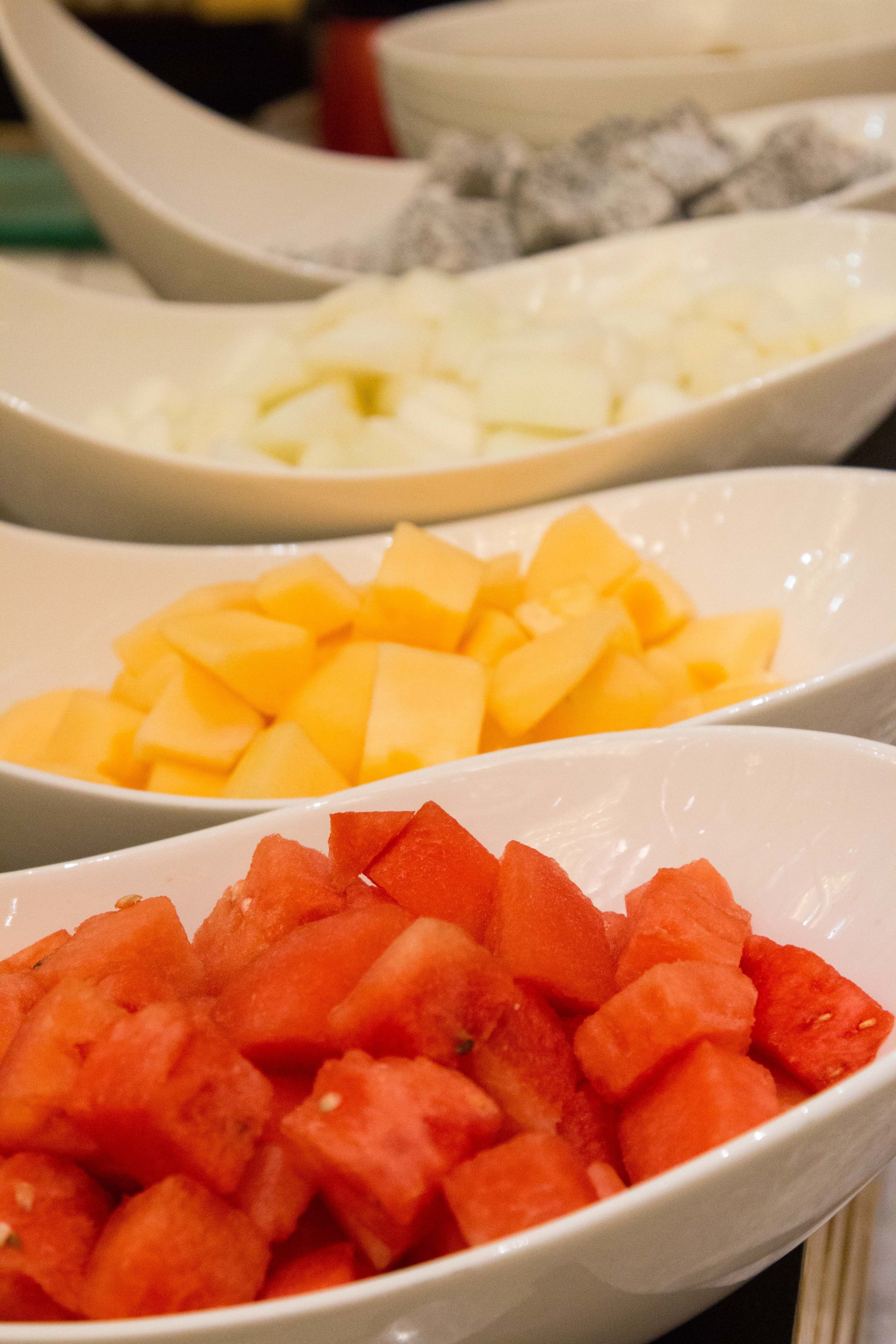 Three white bowls containing diced fruits.