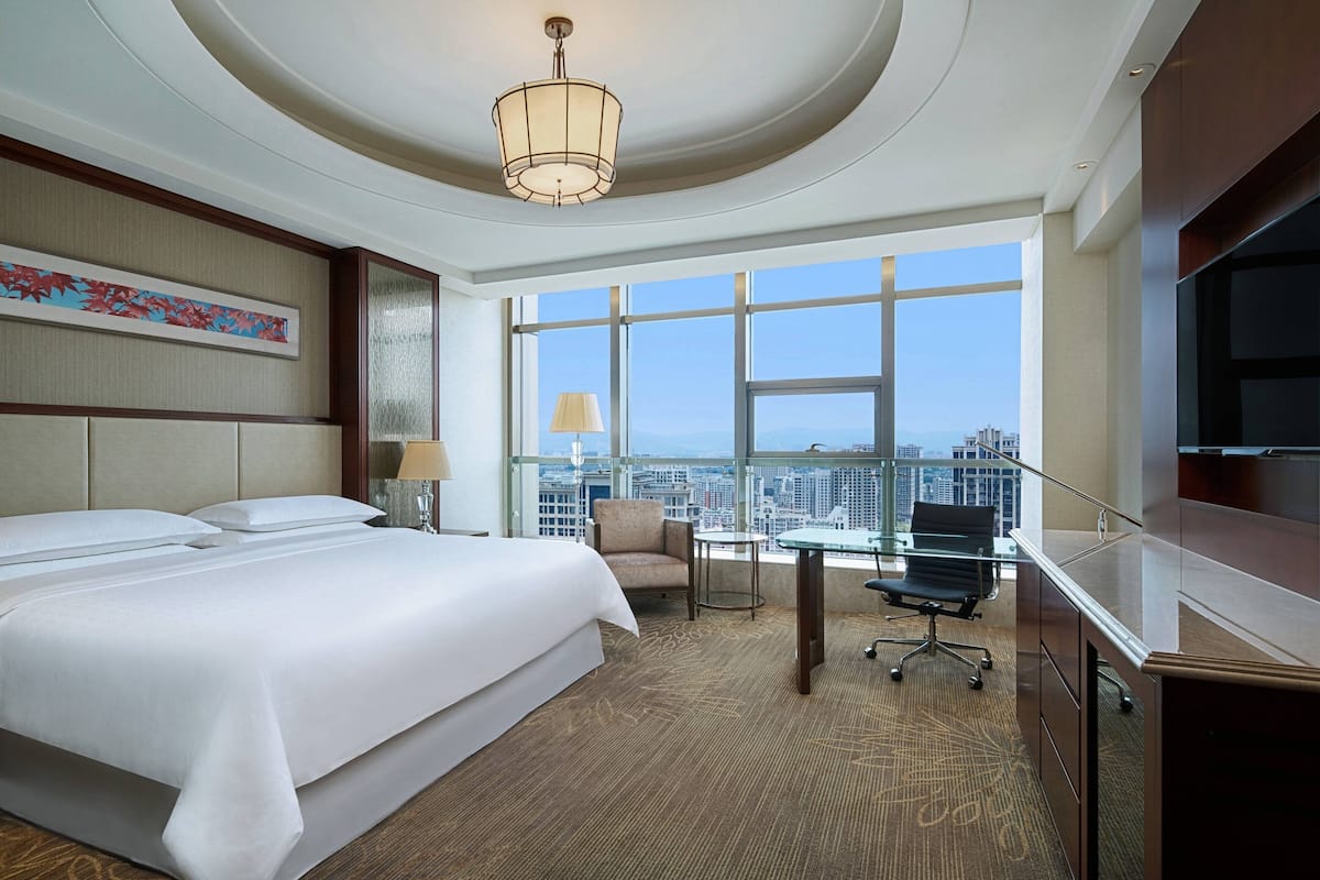 Habitación de hotel con una cama grande, un escritorio, una silla y un televisor. Hay una ventana con vista a la ciudad.