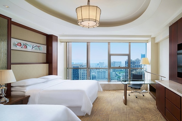 A hotel room with two beds, a desk, a chair, a TV, and a large window offering a city view. - Sheraton Nanchang Hotel (Nanchang)