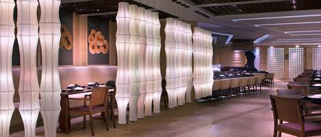 Un restaurante con decoración moderna, que presenta lámparas blancas y abstractas de gran altura y mesas y sillas de madera.
