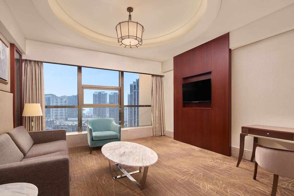 Una habitación de hotel moderna con un ventanal grande, un sofá, una mesa y un televisor.