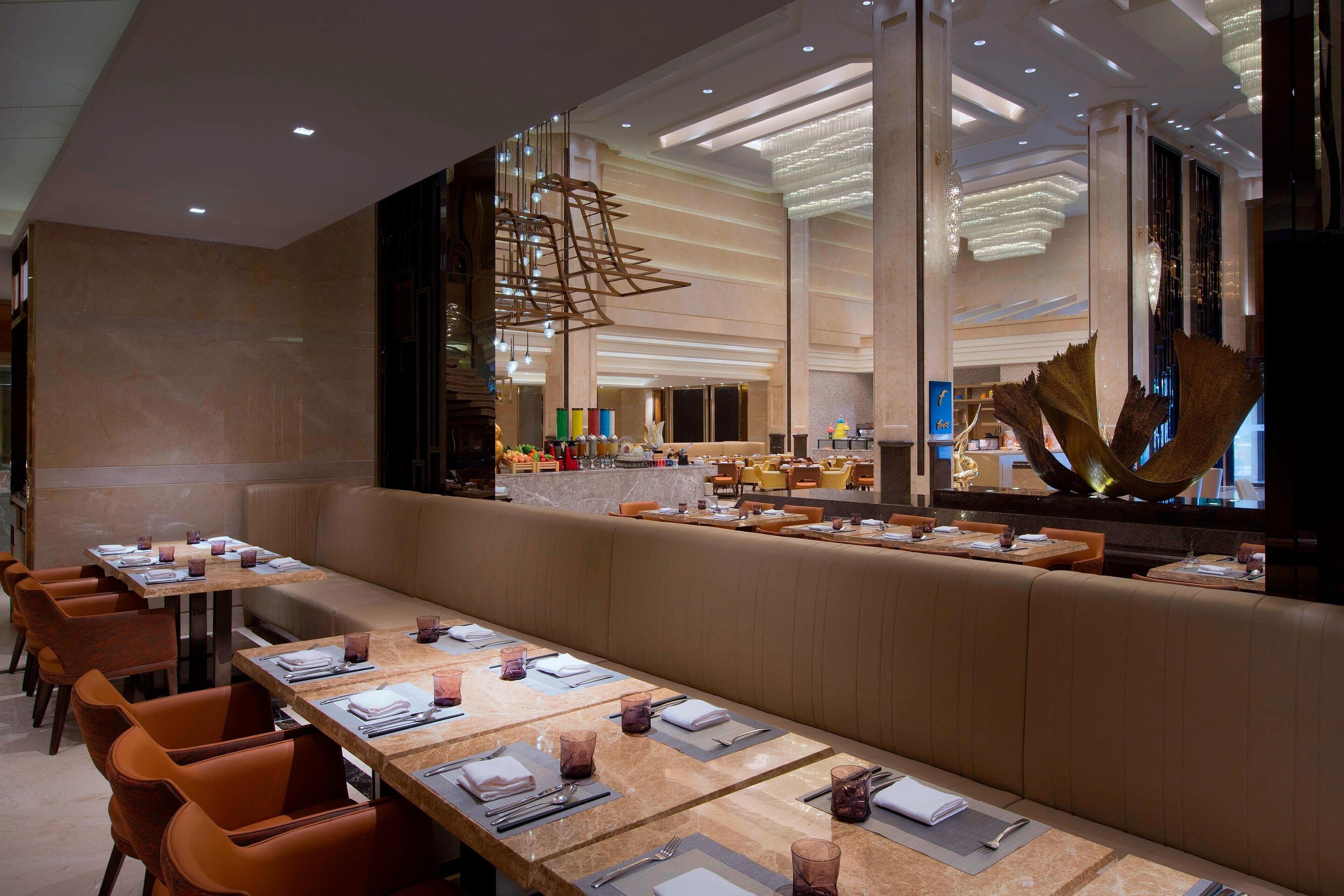 A modern restaurant with long communal tables and booths, high ceilings with recessed lighting, and a large decorative sculpture.