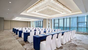 A conference room with rows of tables, white chairs, and a large chandelier.
