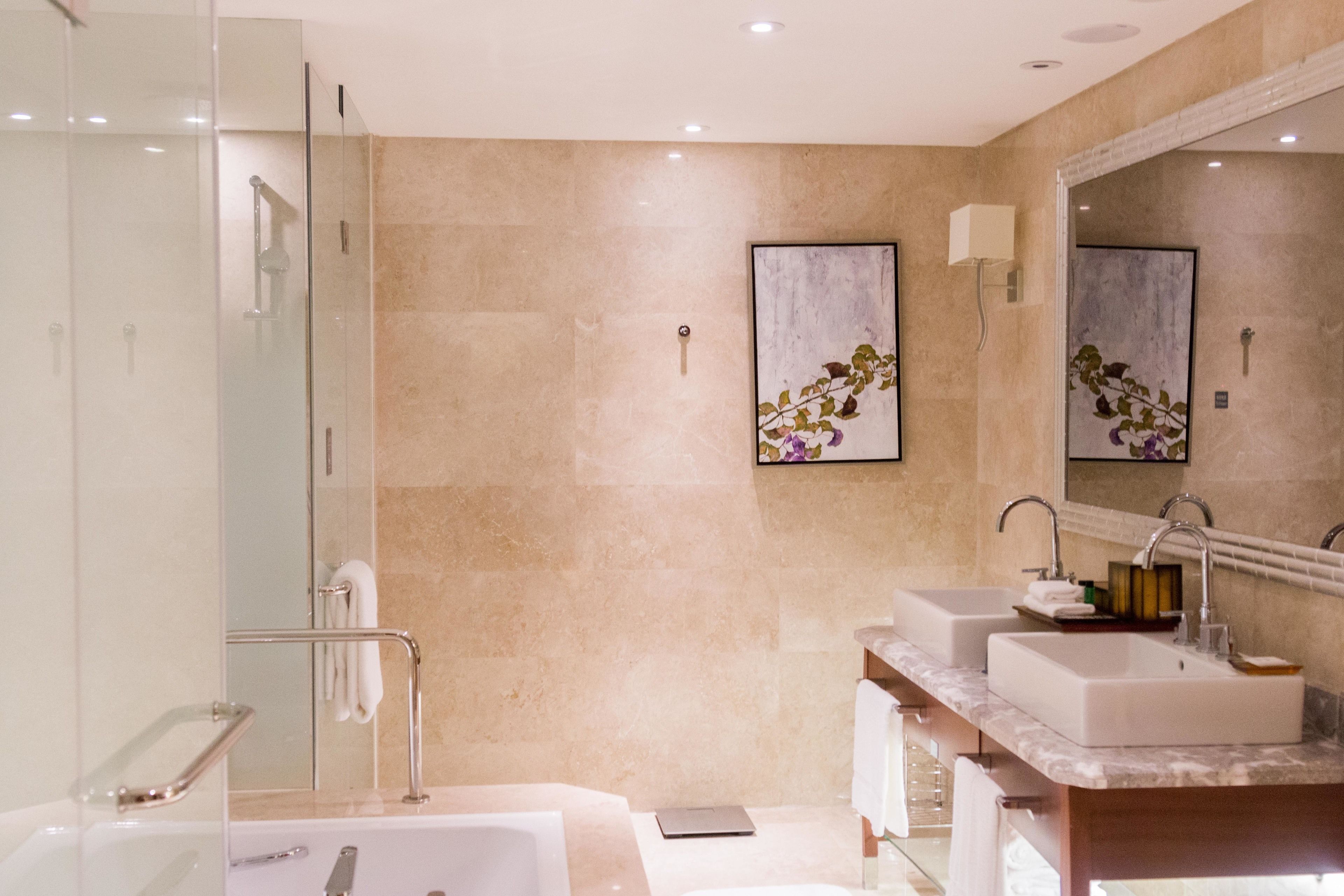 A modern bathroom with a glass-enclosed shower, two sinks, a large mirror, and a marble countertop.