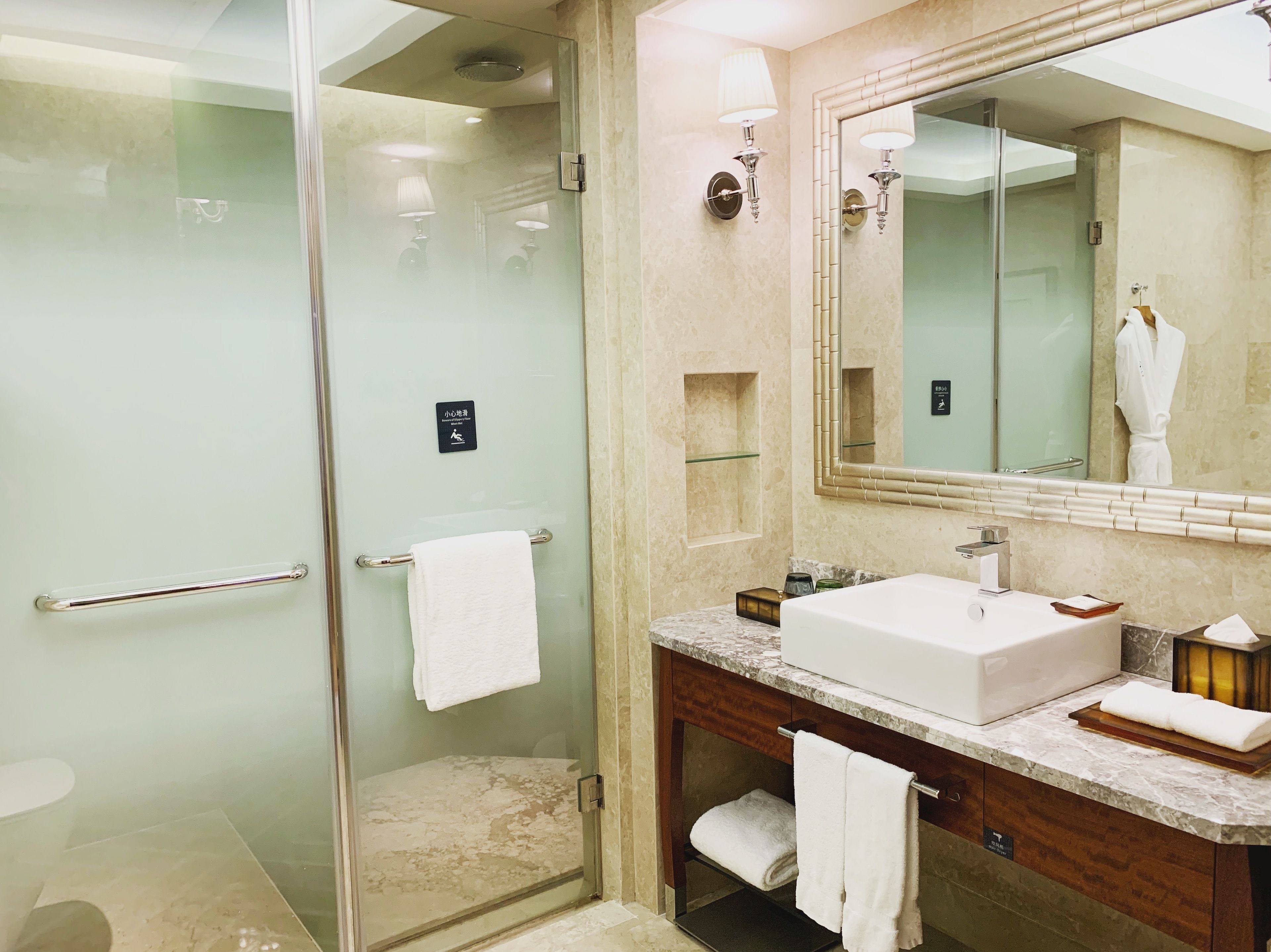 Ein modernes Badezimmer mit einer Glaskabine zur Dusche, einem großen Spiegel, einer Marmorplatte und einem weißen Waschbecken.