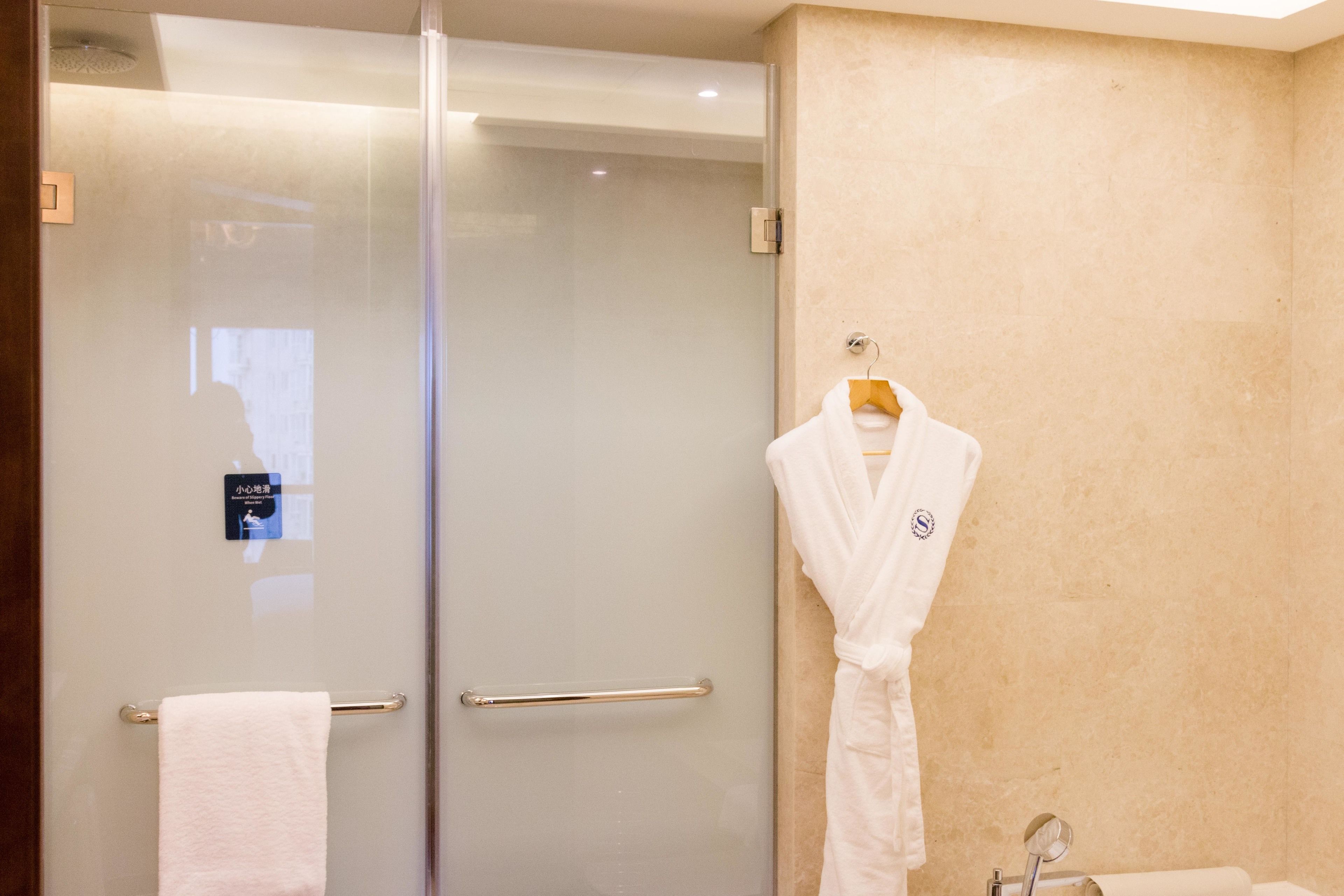 A bathroom with a glass shower door, a towel rack with a white towel, and a white robe hanging on a hook.