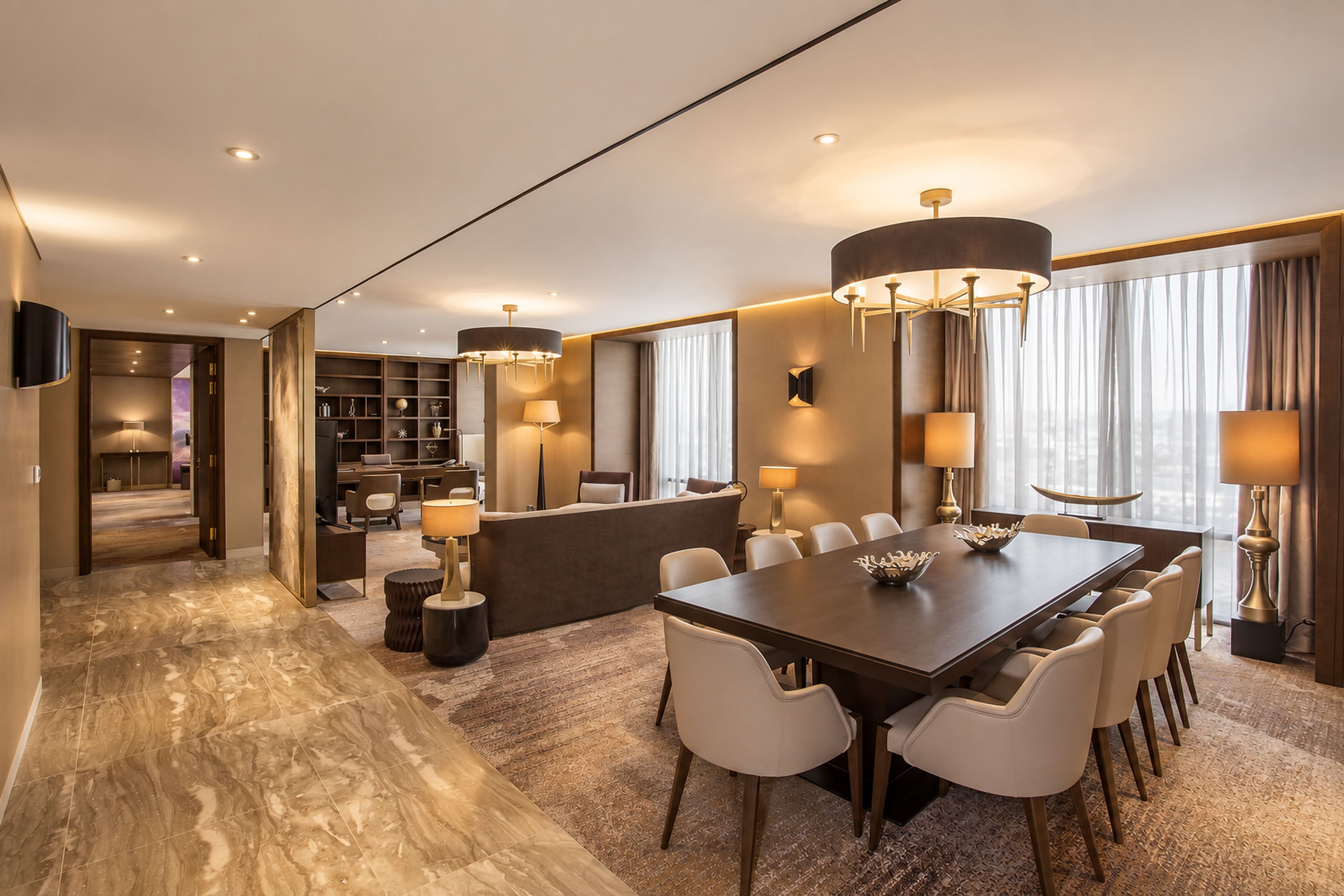 Una habitación de hotel moderna con zona de comedor, mostrador de recepción y vistas a la ciudad.