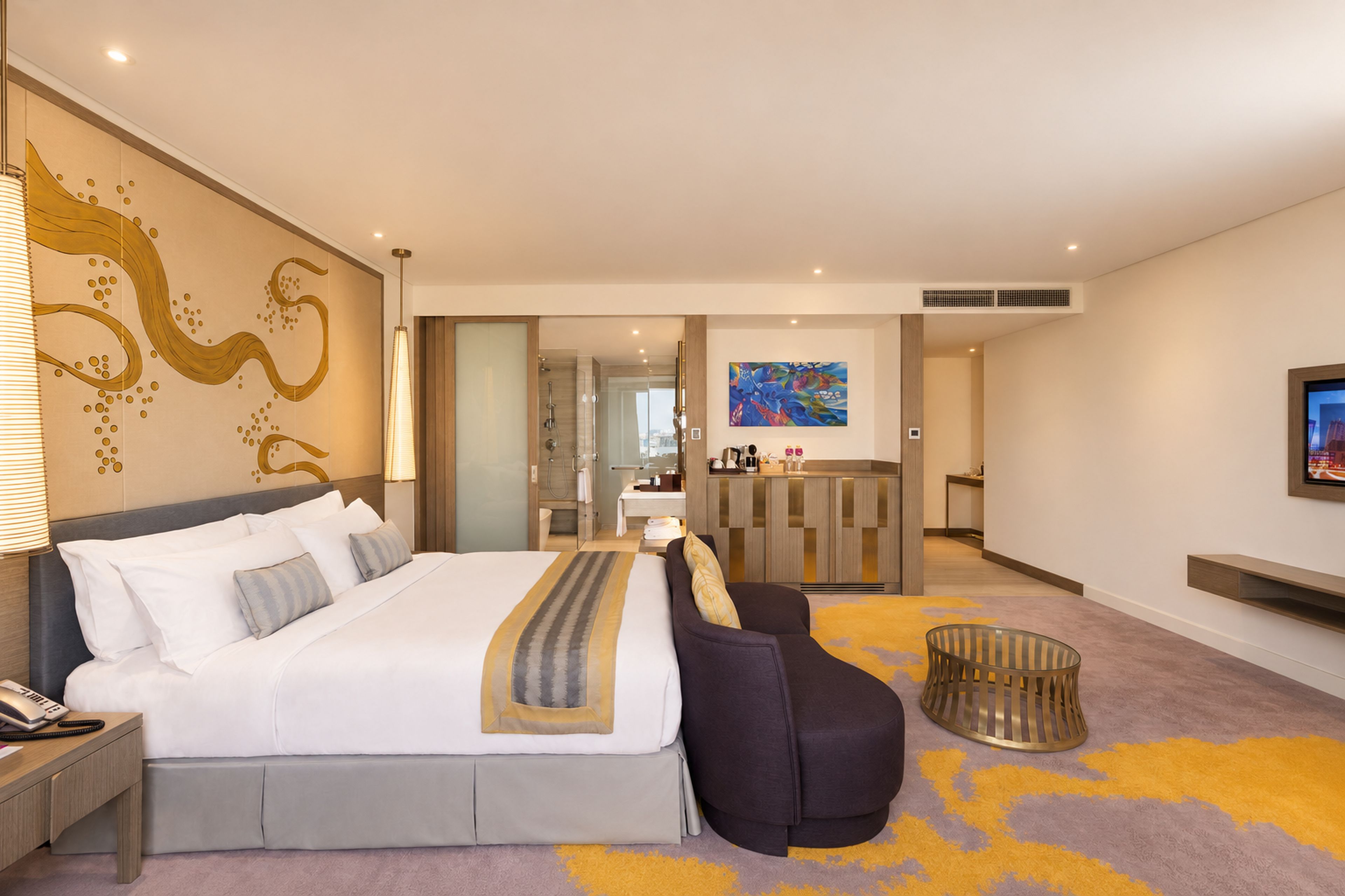 Habitación de hotel con una cama grande, un sofá, un escritorio, un baño y un televisor en la pared.