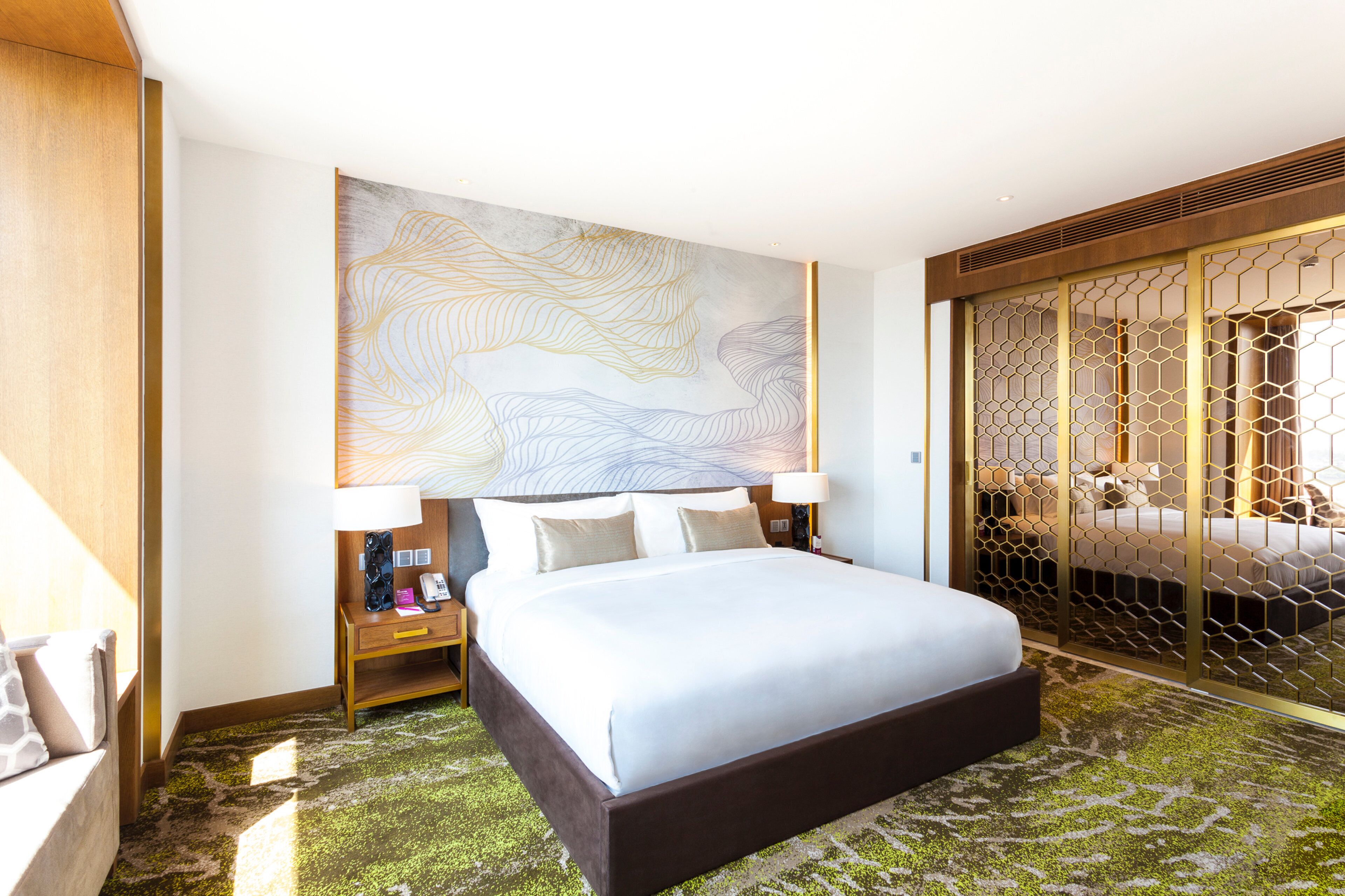 A hotel room with a large bed, a nightstand, a wall-mounted lamp, and a decorative wall piece.
