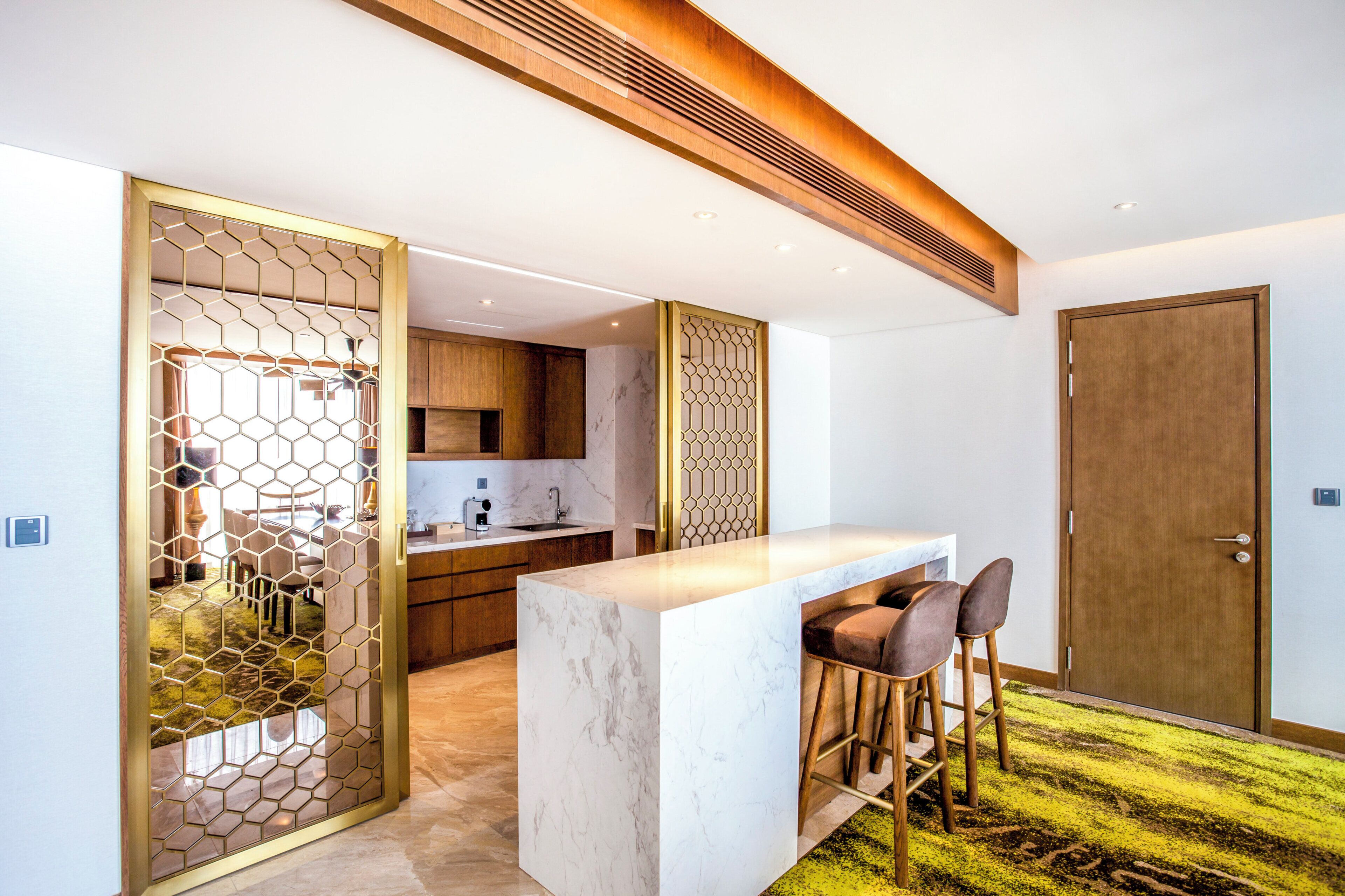 A modern kitchen with a marble countertop, wooden cabinets, and a decorative hexagonal partition.