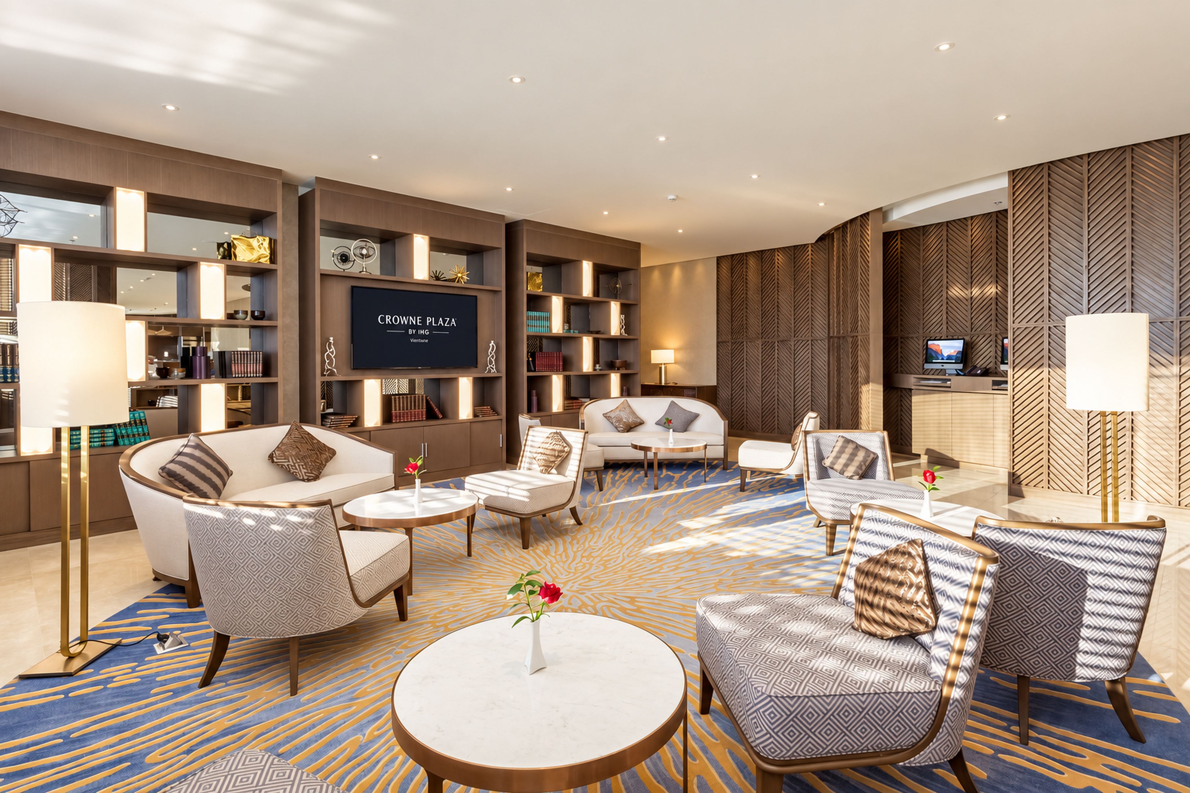 A modern hotel lobby with a seating area, a television, and a bookshelf.
