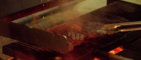 Una parrilla con carne asándose sobre llamas abiertas.