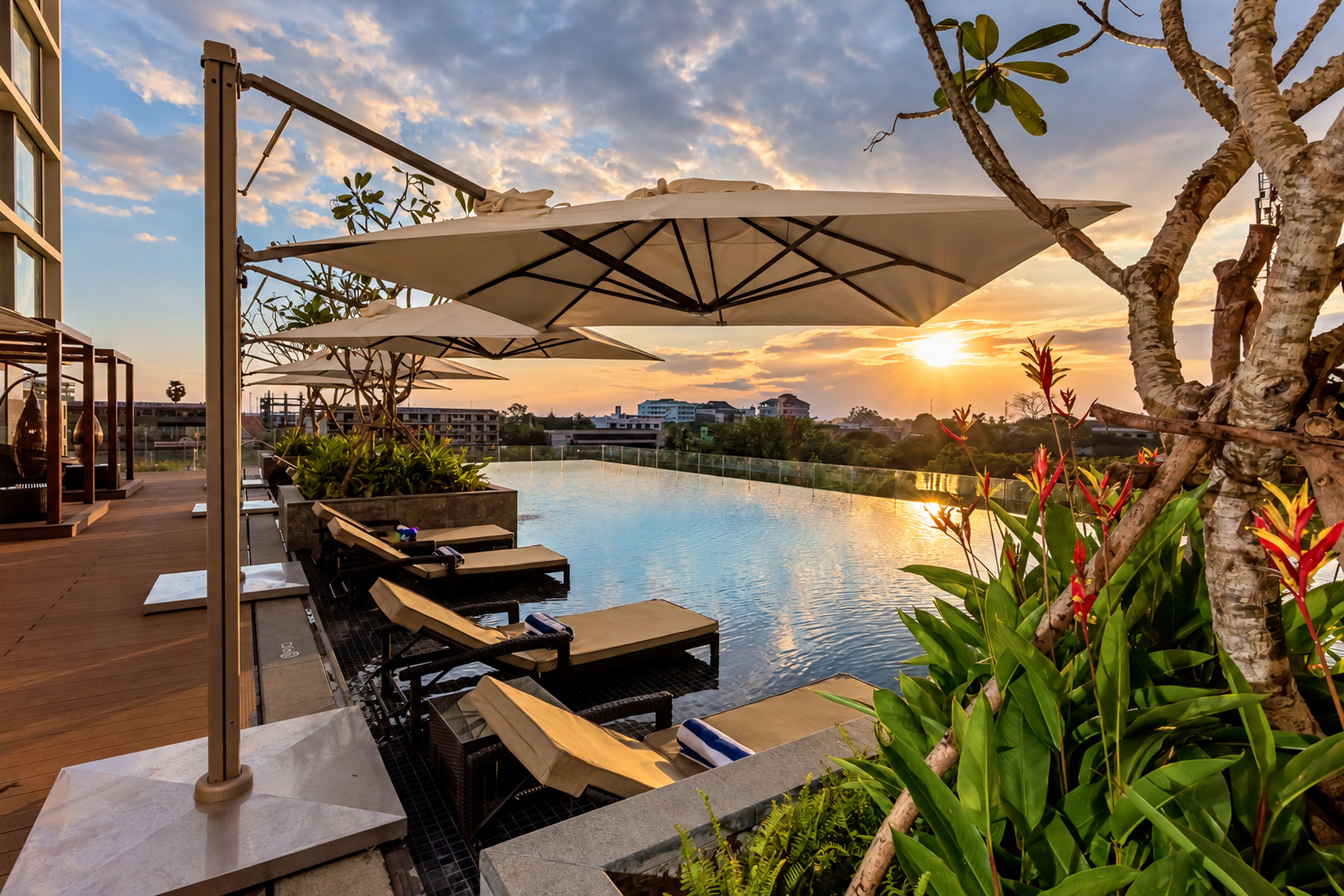Un área junto a la piscina con sillones de descanso, sombrillas y vistas a la puesta de sol sobre el agua.