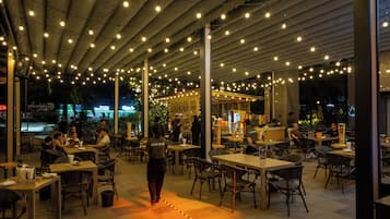 An outdoor dining area with tables and chairs, string lights overhead, and a central walkway.