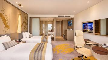 Une chambre d’hôtel avec deux lits, un bureau, une chaise, une télévision et une salle de bain visible à travers une porte ouverte.