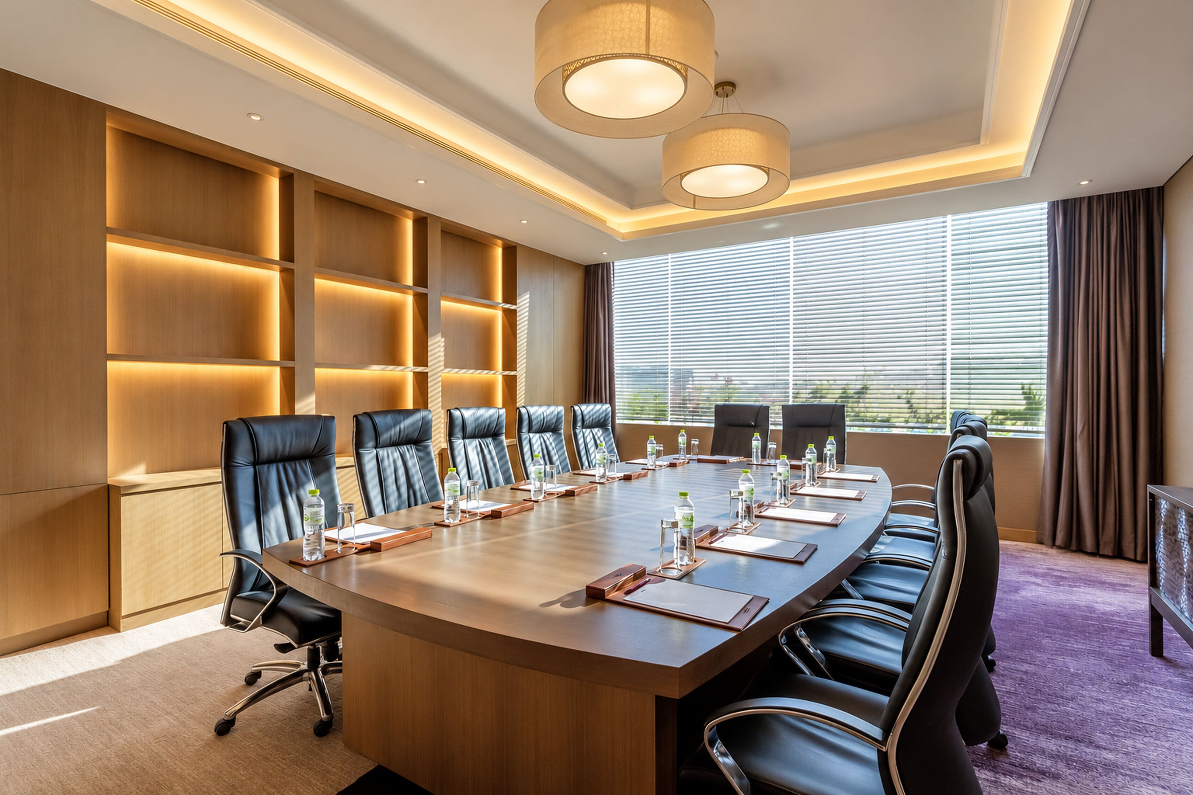 Une salle de conférence avec une longue table, de nombreuses chaises et une grande fenêtre équipée de stores.