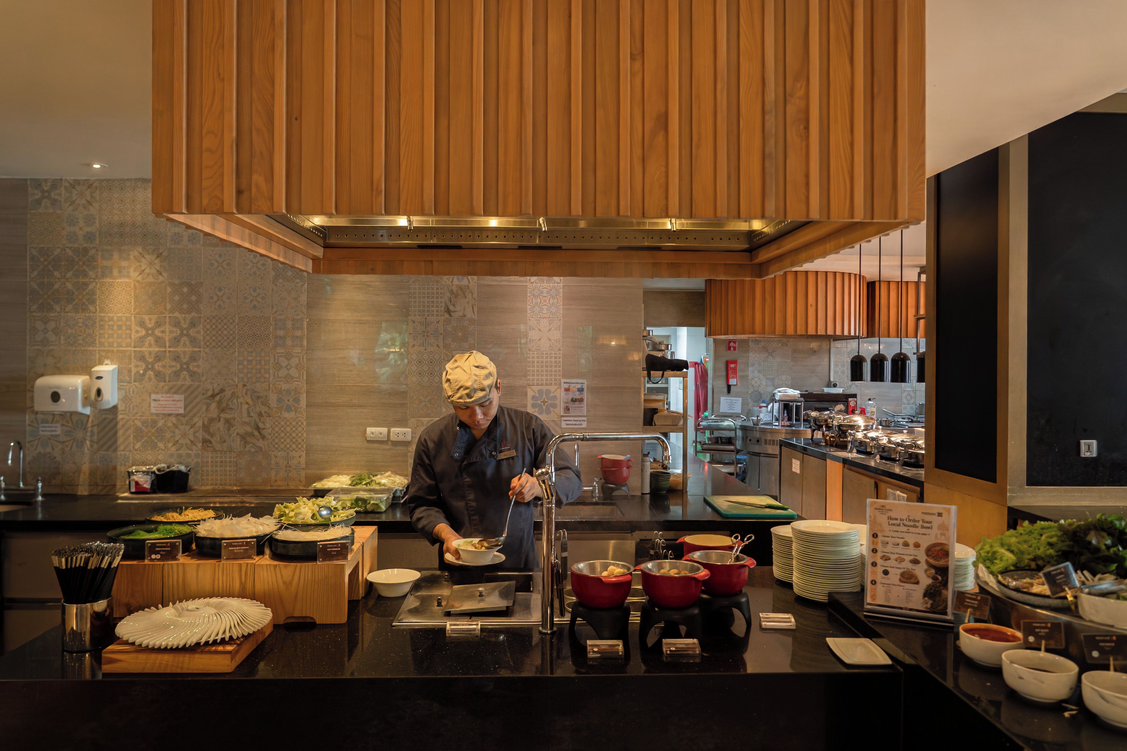 A chef preparing food in a modern kitchen with wooden cabinets and a tiled backsplash.