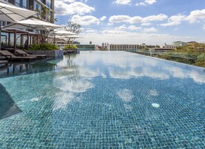 A large, clear blue infinity pool with lounge chairs and umbrellas, surrounded by buildings and a clear sky. - Crowne Plaza Vientiane by IHG (Vientiane)