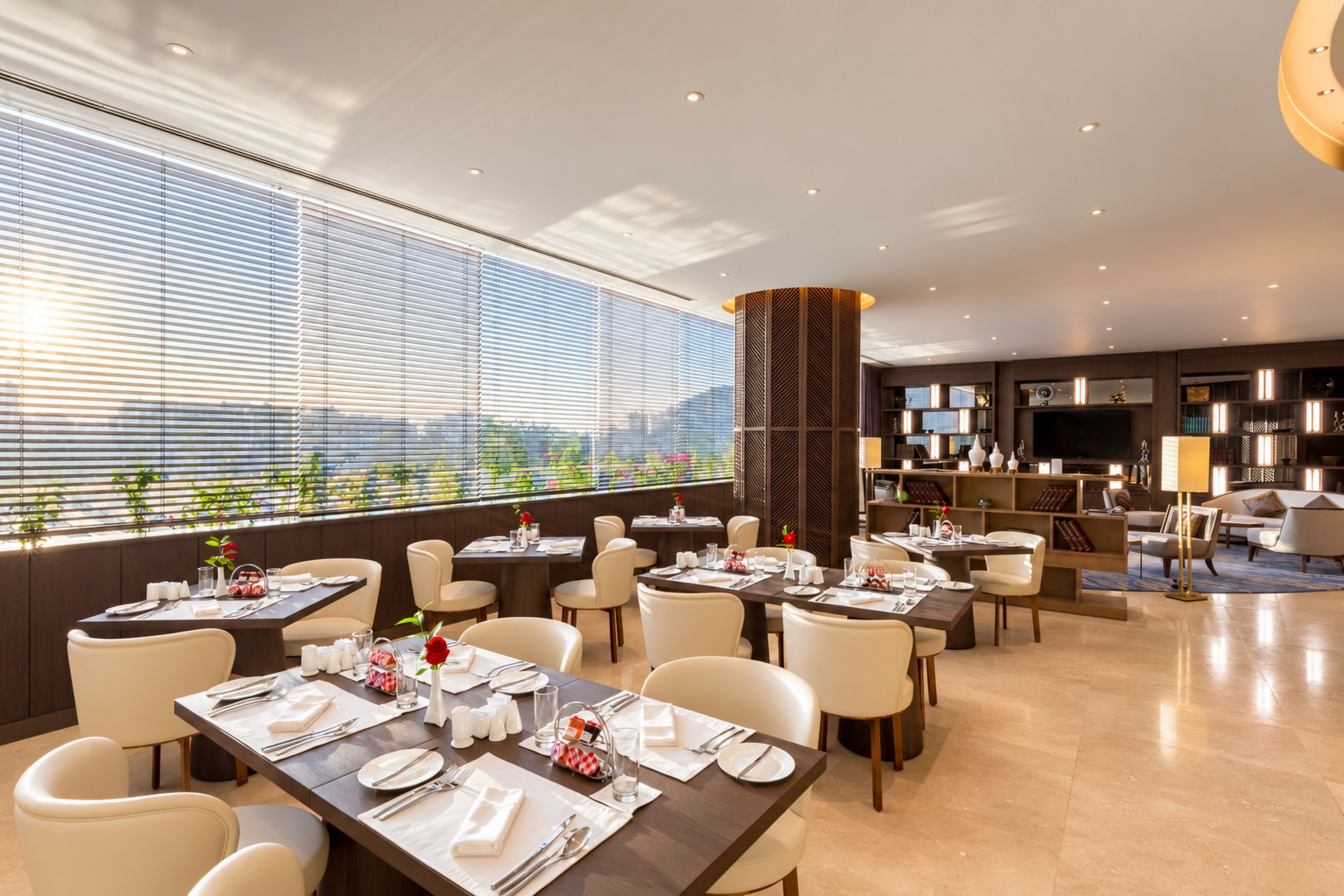 A modern dining area with tables set for service, a large window with blinds, and a view of the cityscape.