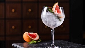 A glass of a clear, icy beverage garnished with a slice of grapefruit and a sprig of rosemary, placed on a dark surface with a wooden background. - Crowne Plaza Vientiane by IHG (Vientiane)