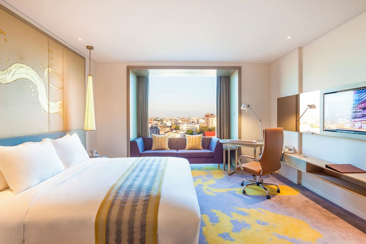 A hotel room with a large bed, a sofa, a desk, and a TV.