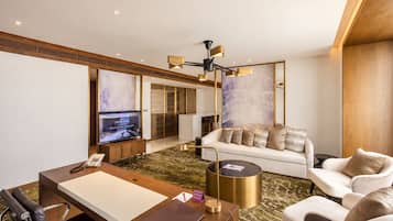 Ein modernes Hotelzimmer mit einer Couch, einem Schreibtisch mit Telefon, einem Couchtisch und einem Fernseher, der eine Willkommensnachricht zeigt.