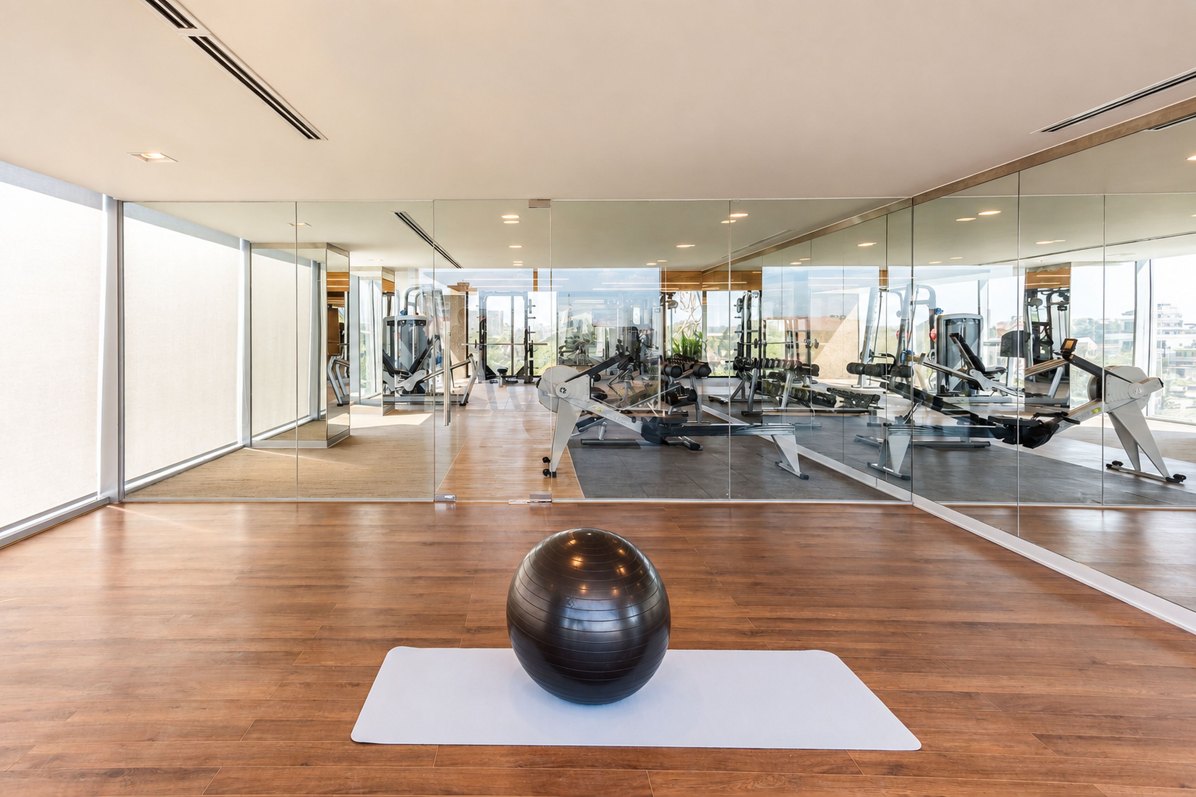 Ein modernes Fitnessstudio mit Trainingsgeräten, großen Fenstern und Holzboden.