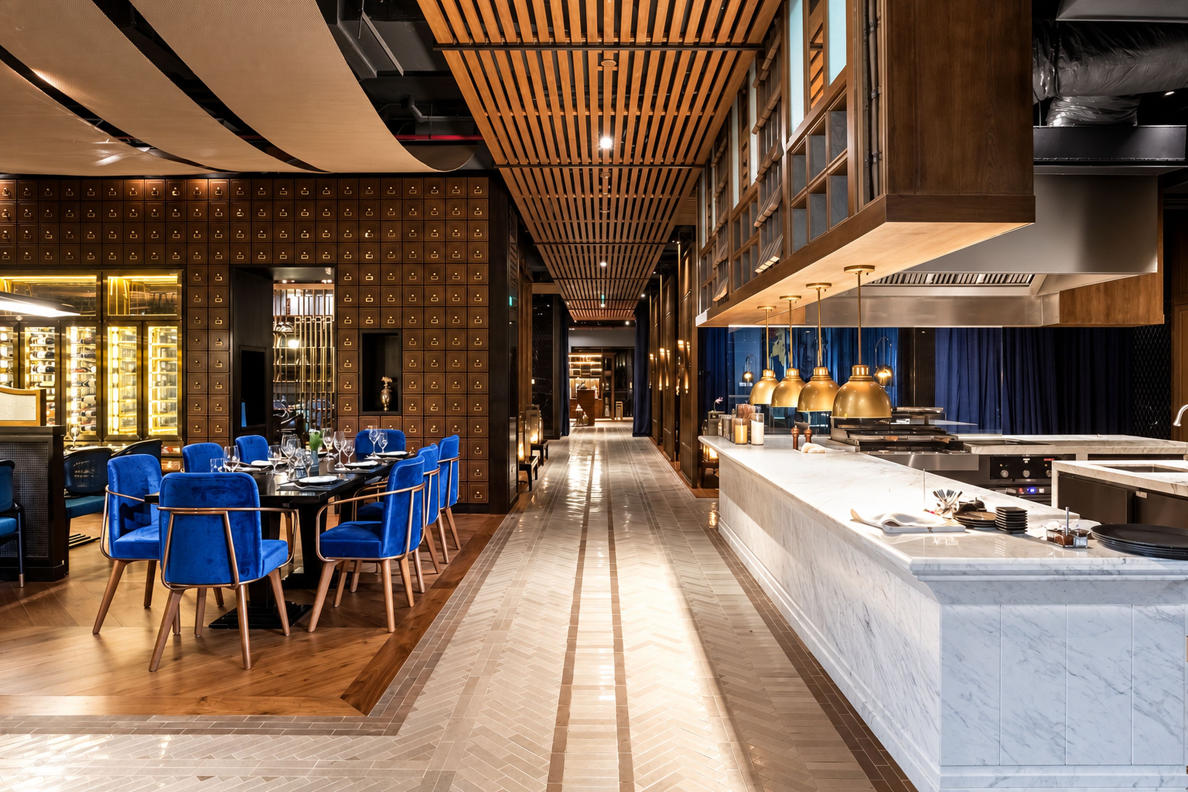 A modern hotel lobby with a long corridor, a dining area with blue chairs, and a kitchen with stainless steel appliances.