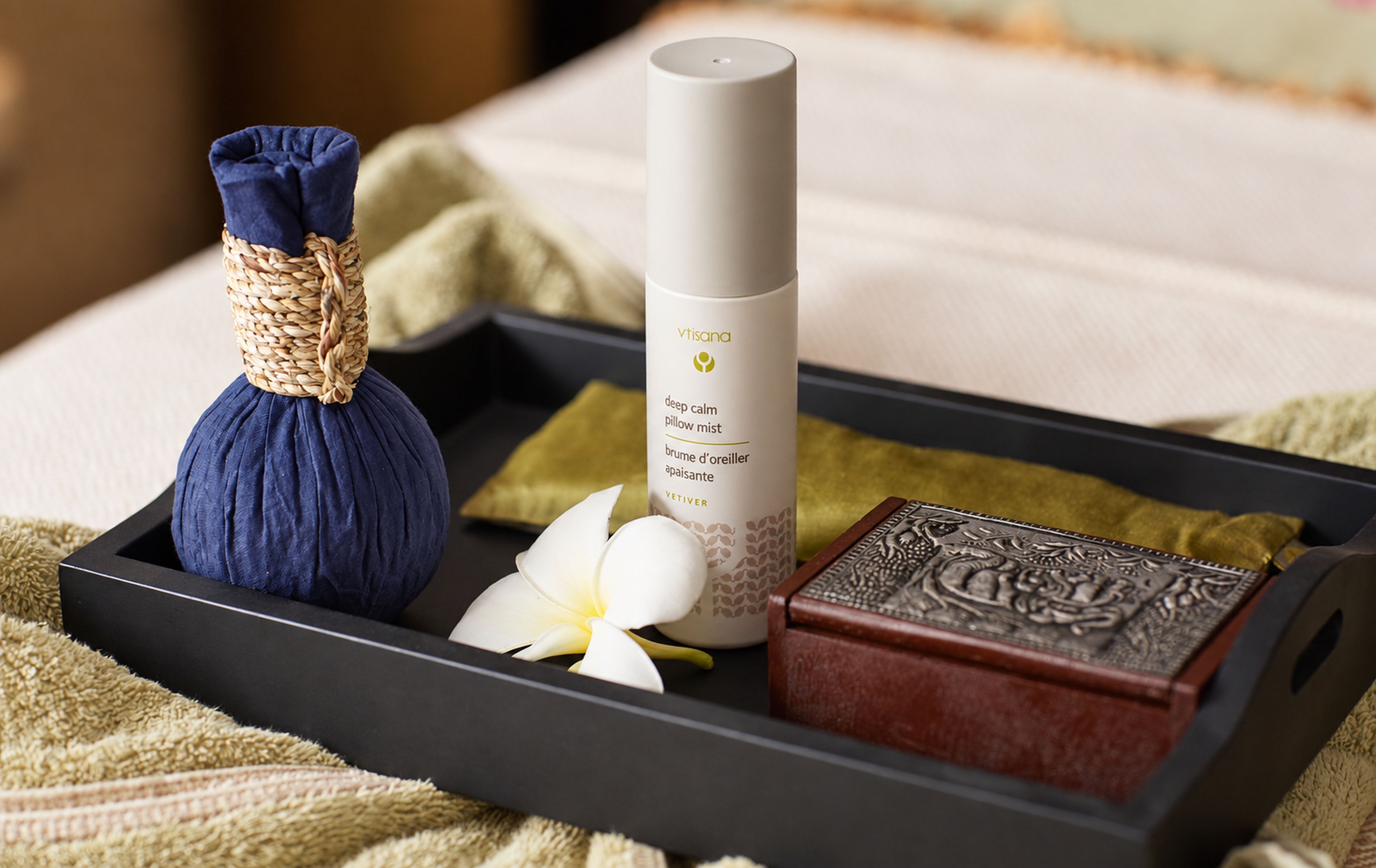 A tray with a blue massage ball, a white bottle labeled 'deep calm pillow mist,' a white flower, and a wooden object.