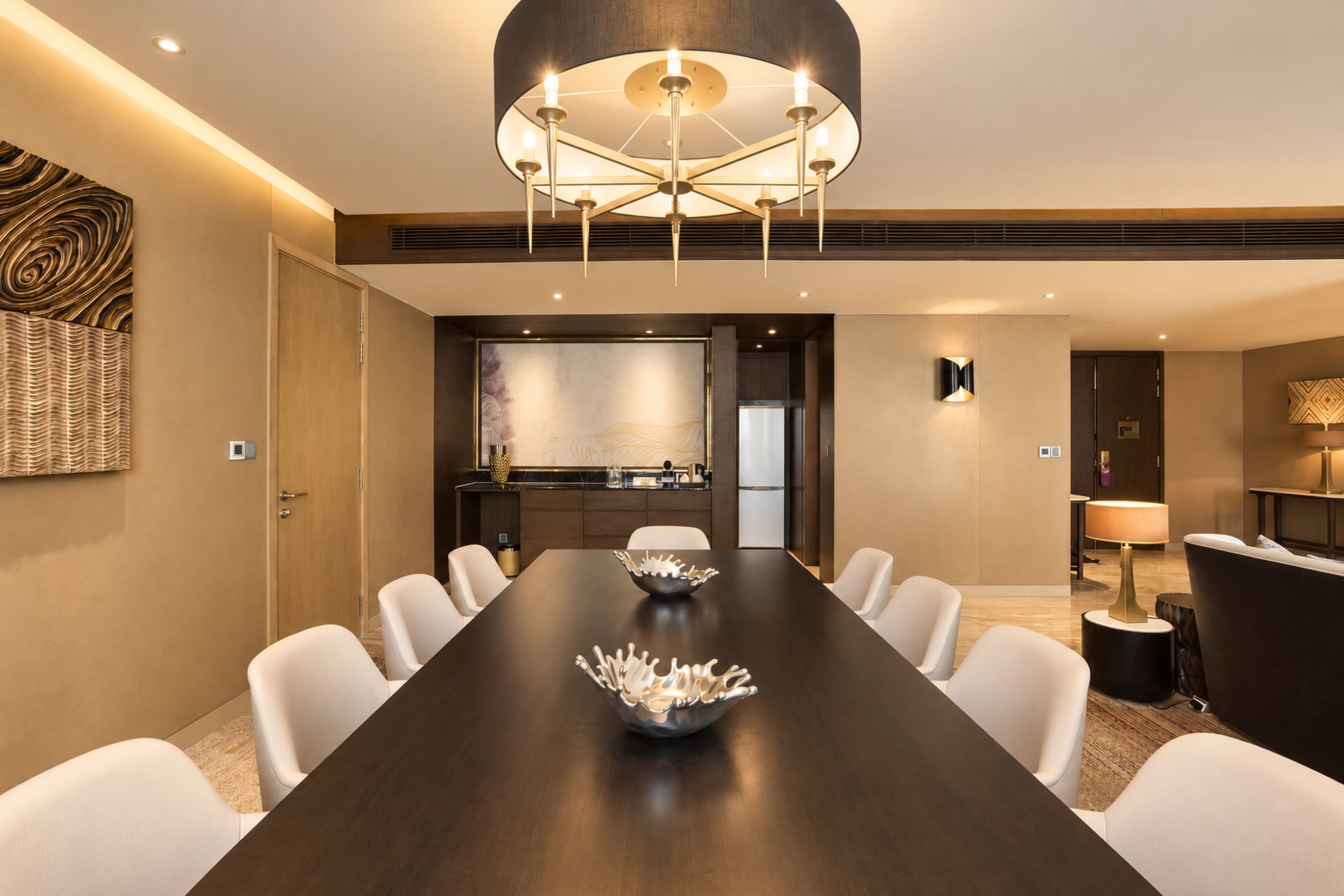 A modern conference room with a long table, white chairs, a decorative bowl, and a unique ceiling light fixture.