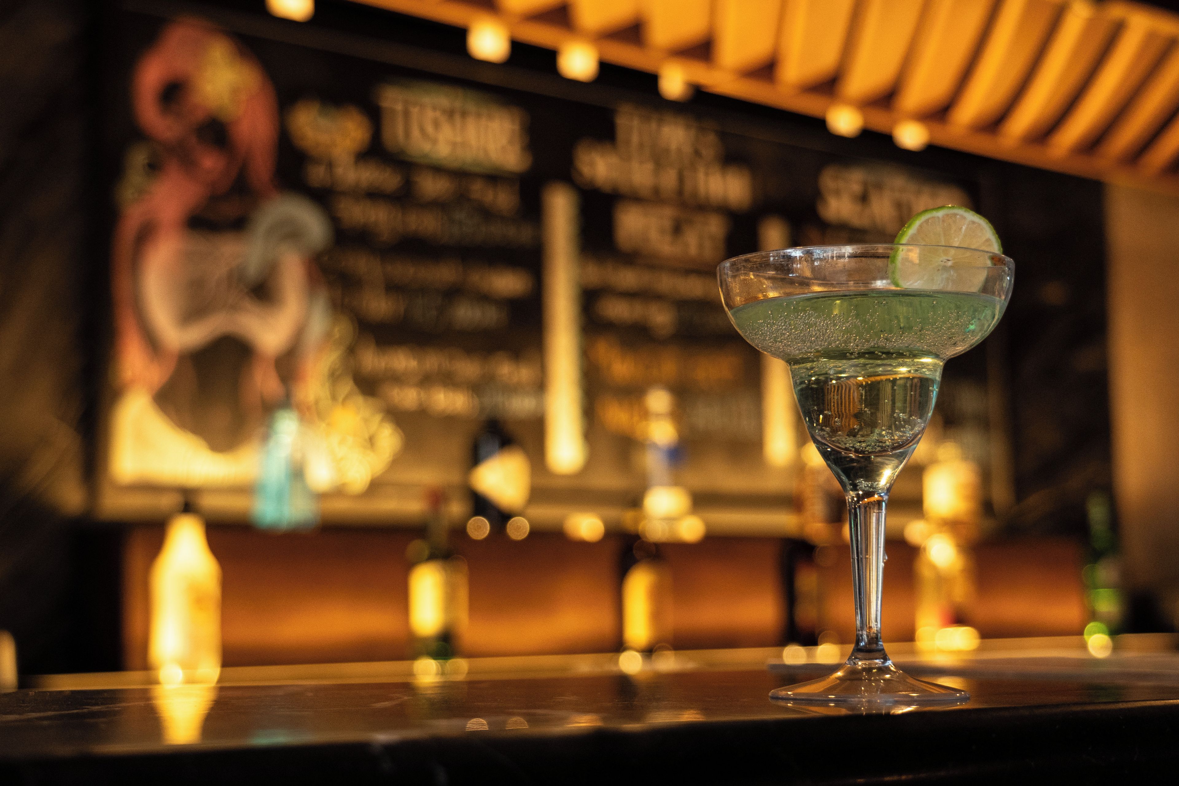 Un verre à cocktail, garni d’une tranche de citron vert, posé sur le comptoir d’un bar.