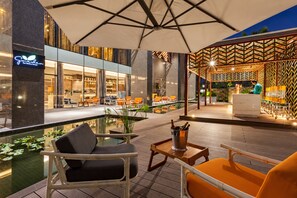 An outdoor seating area with tables and chairs, a pool, and a bar area with a patterned wall. - Crowne Plaza Vientiane by IHG (Vientiane)
