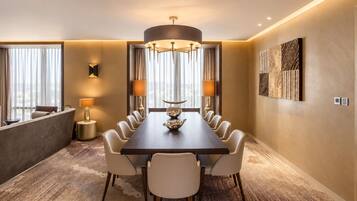 Une salle à manger d’hôtel avec une longue table, des chaises, un lustre et une grande fenêtre avec des rideaux.